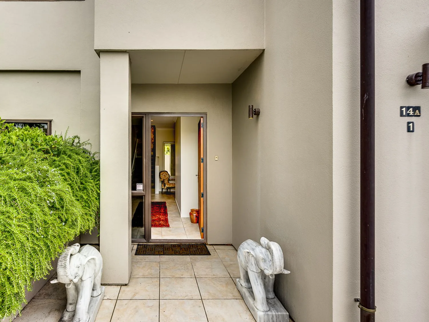 An entrance area with tiled floor two elephant statues and an open doorway showing a hallway with a red rug and a chair at Busby Hill Villa - Havelock North Holiday Home in Havelock North