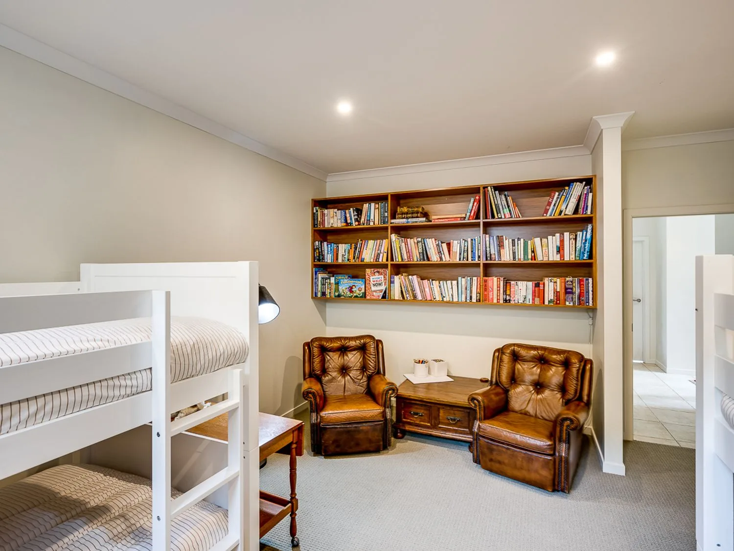 A bedroom with white bunk beds leather armchairs wooden table and a wall-mounted bookshelf at Busby Hill Villa - Havelock North Holiday Home in Havelock North