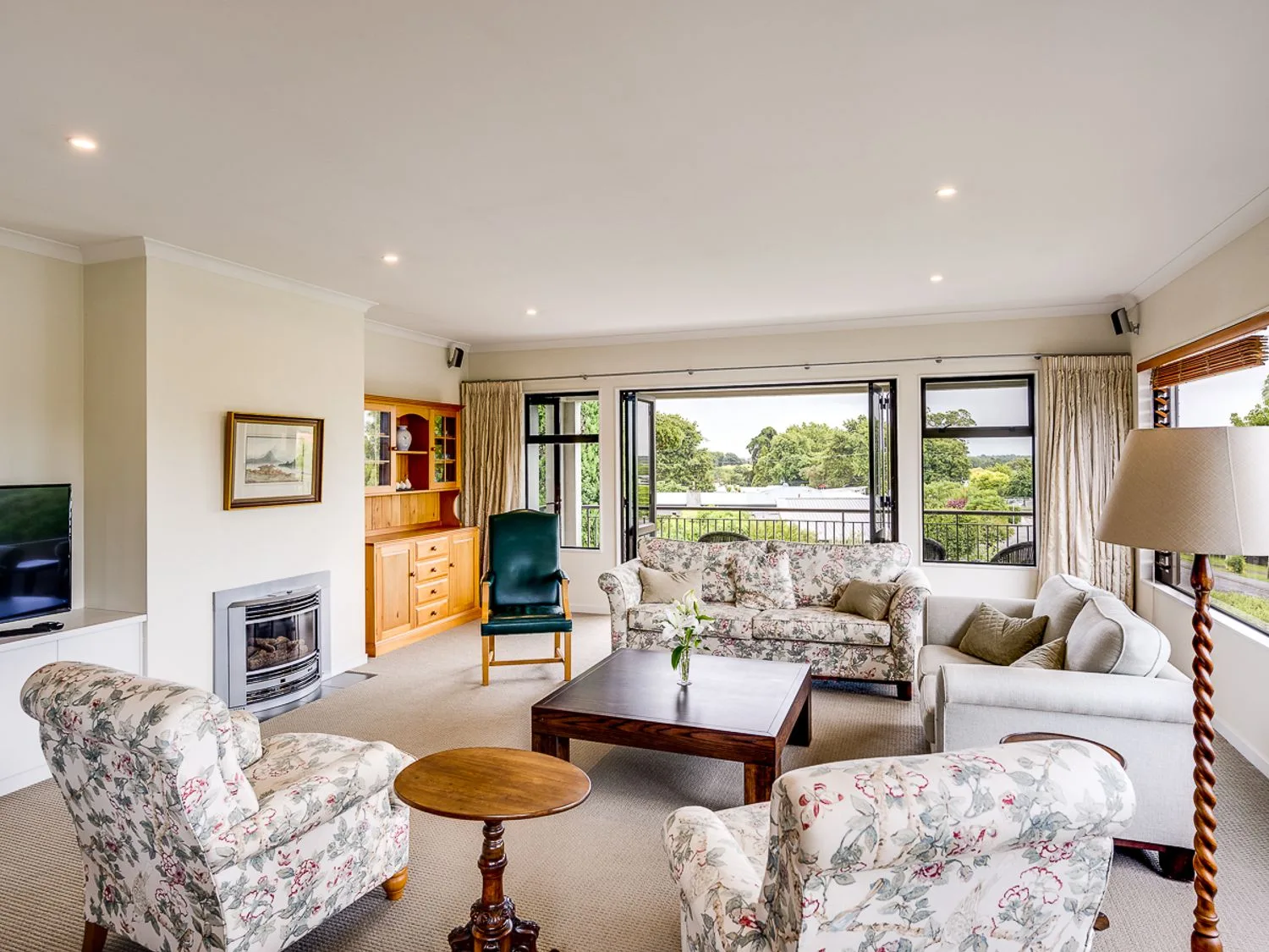 A living room with floral armchairs a beige sofa a wooden coffee table a floor lamp and large windows at Busby Hill Villa - Havelock North Holiday Home in Havelock North