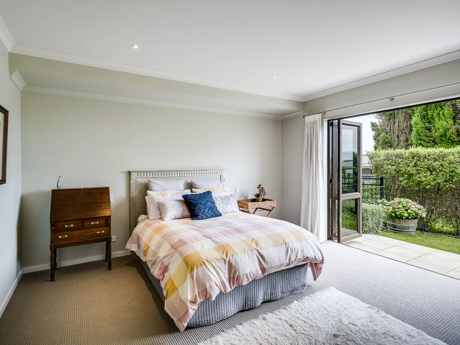 A bedroom with a bed a wooden cabinet a small table and open doors leading to a garden at Busby Hill Villa - Havelock North Holiday Home in Havelock North