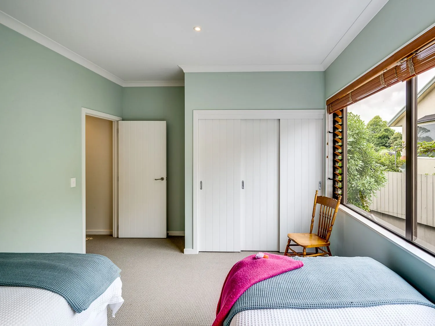 A bedroom with two single beds a wooden chair built in wardrobe and a large window at Busby Hill Villa - Havelock North Holiday Home in Havelock North