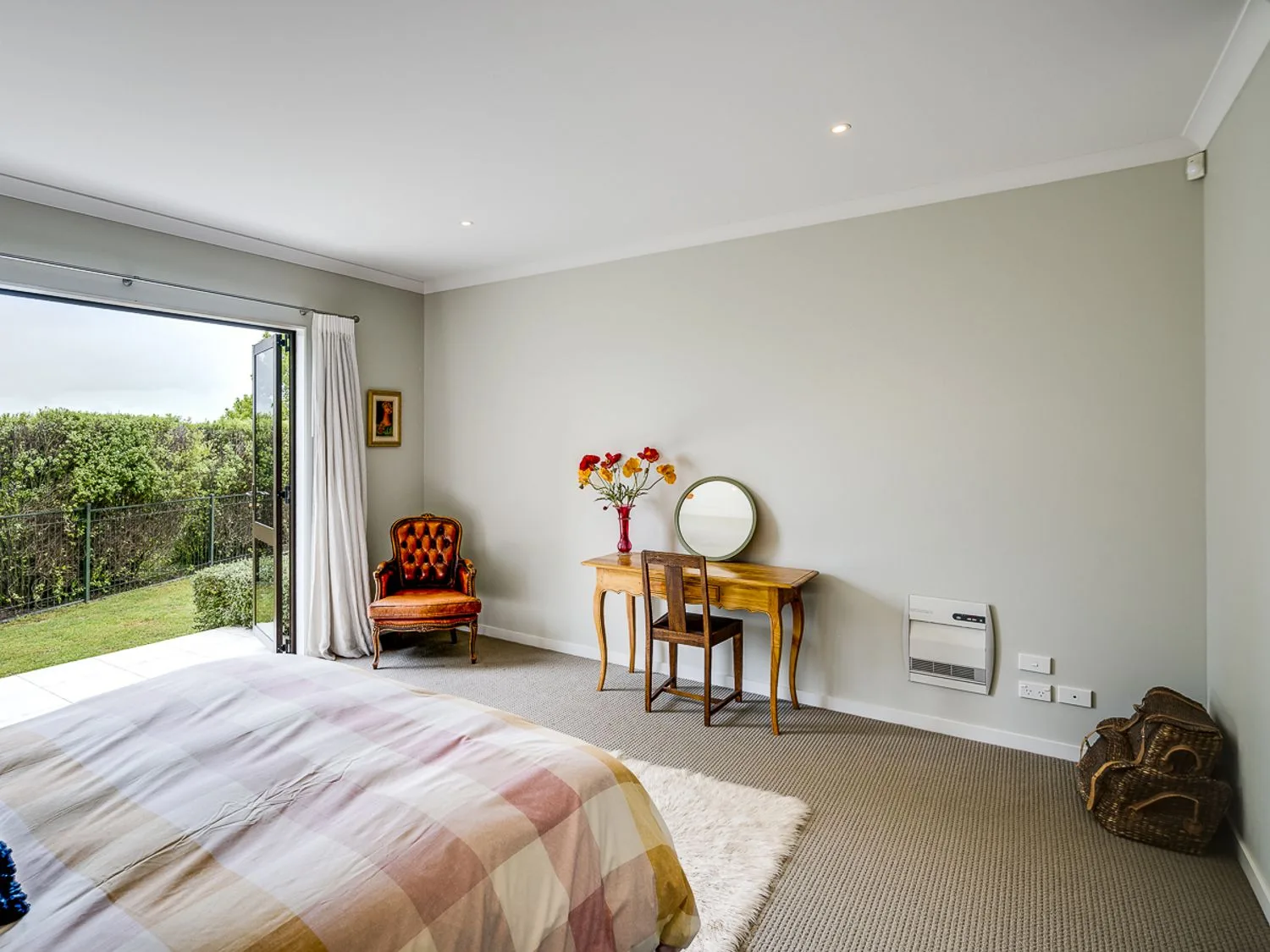 A bedroom with a bed, wooden desk and chair, armchair, and open door to the garden at Busby Hill Villa - Havelock North