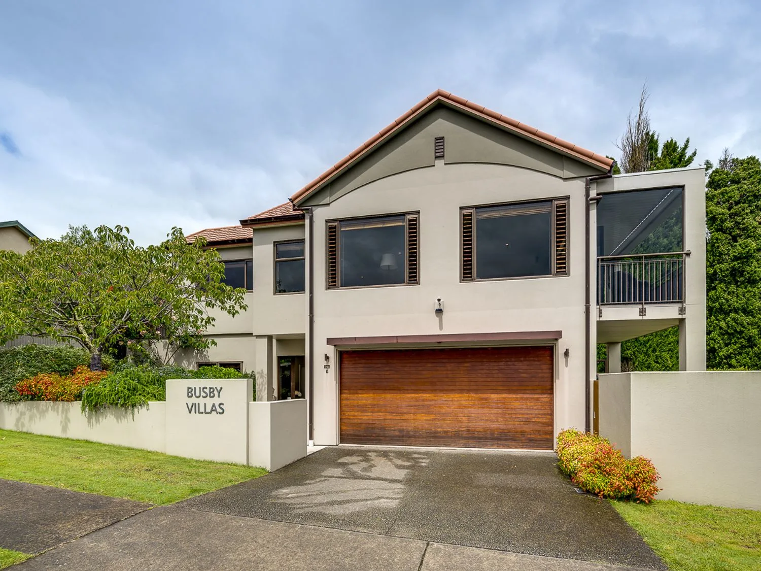 A two-story house with a wooden garage door and a sign that reads busby villas at Busby Hill Villa in Havelock North