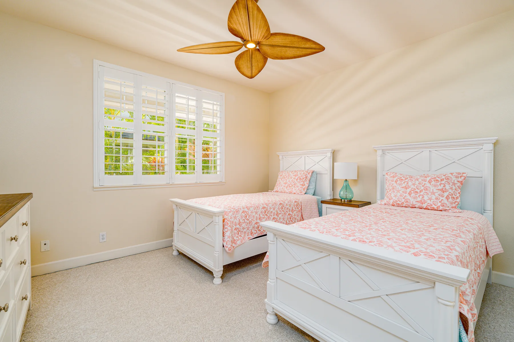A bright bedroom with two beds, floral bedding, and a ceiling fan.