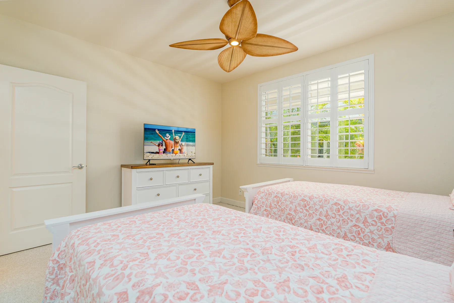 A bright bedroom with two beds, a dresser, and a large window.