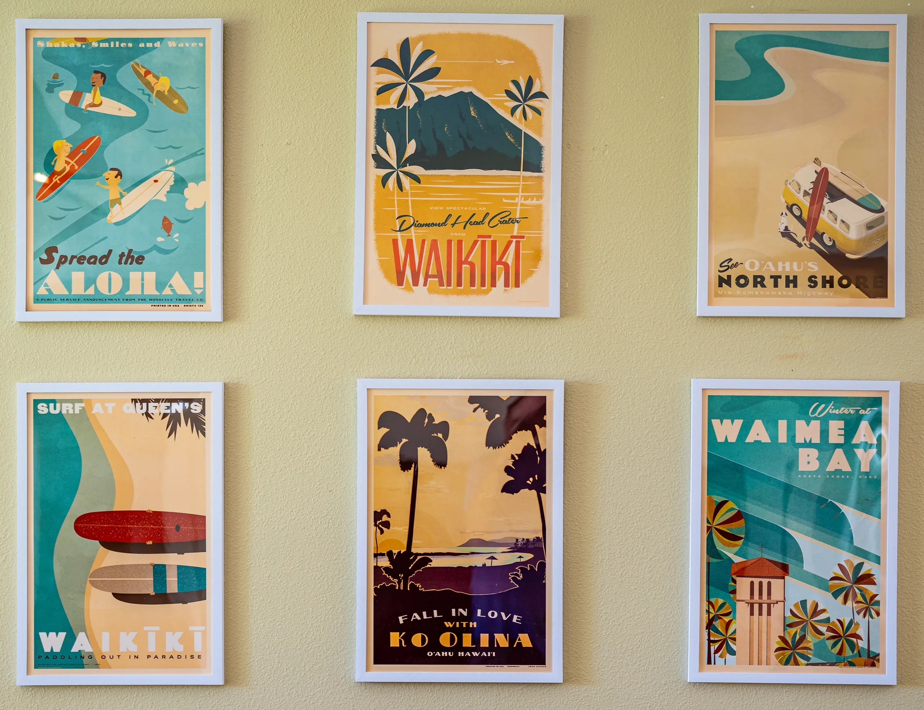 Six colorful framed beach posters hang in two rows on a pale wall.