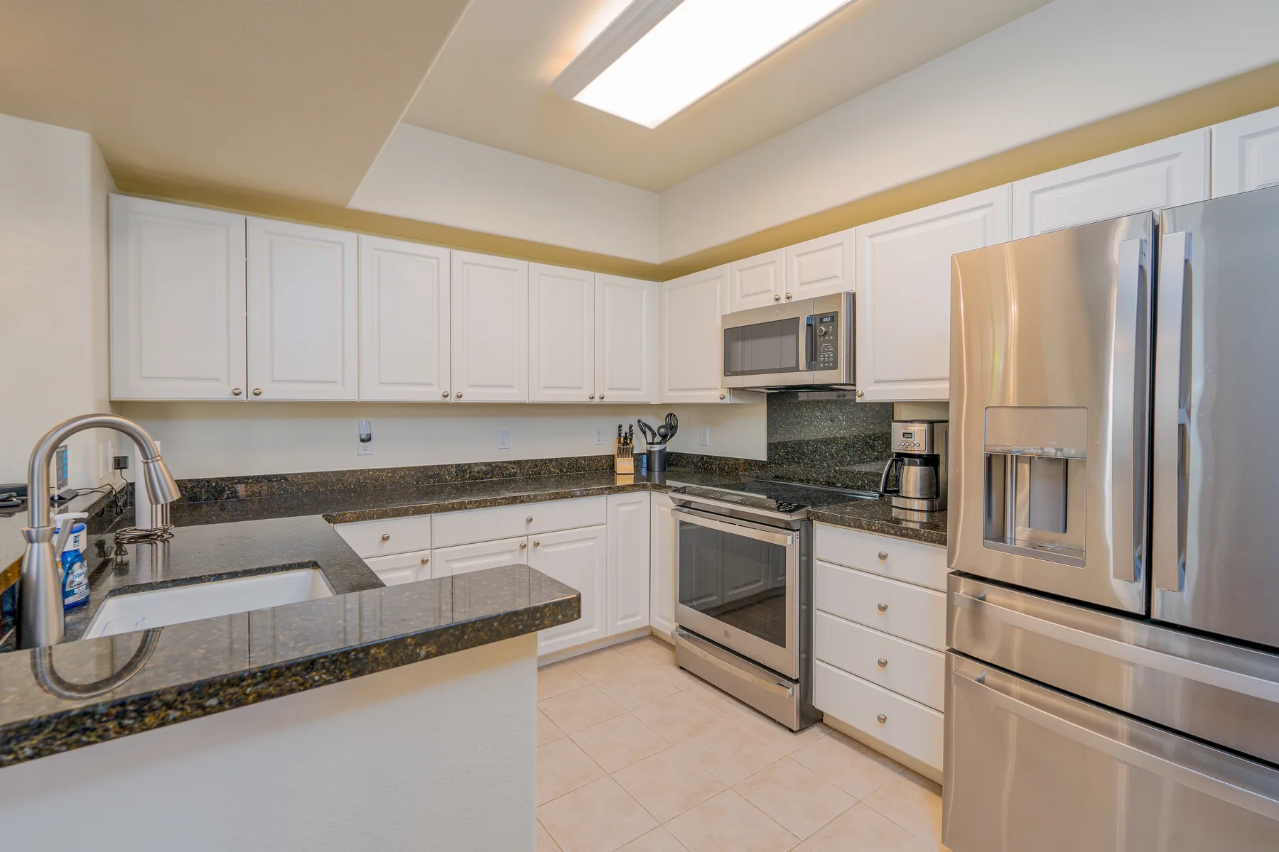 A bright kitchen with white cabinets, stone countertops, and stainless steel appliances.