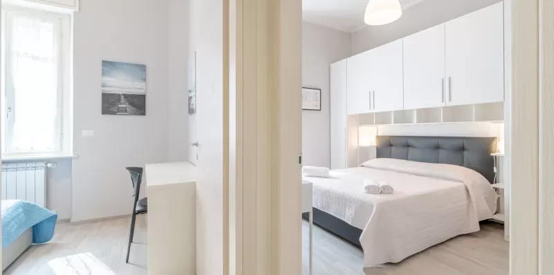 A bright bedroom with a bed, white built-in cabinets, and a small desk.