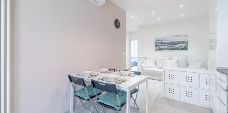A bright dining area with a table and seating beside a living area.