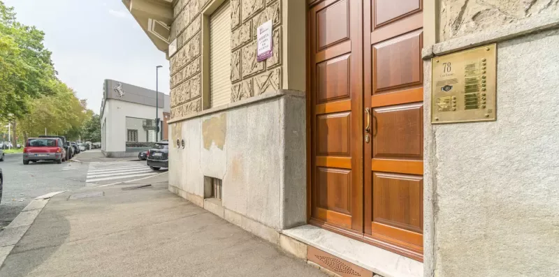 Building entrance with wooden double doors beside a paved sidewalk.