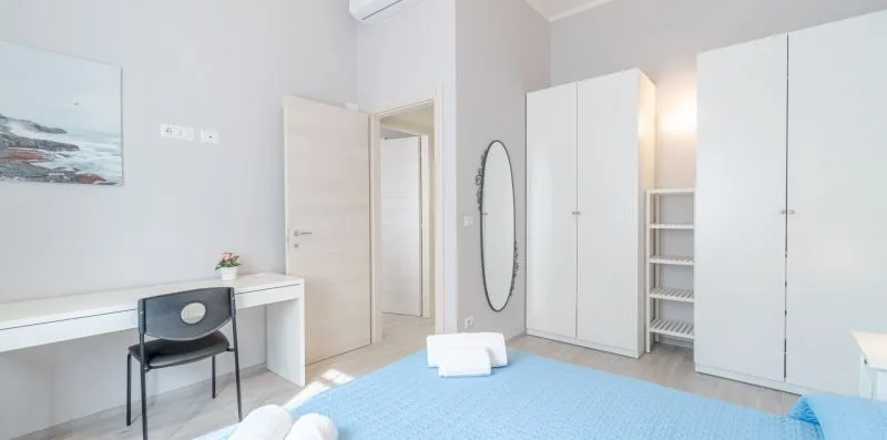 A bright bedroom with a desk, chair, and white storage cabinets.