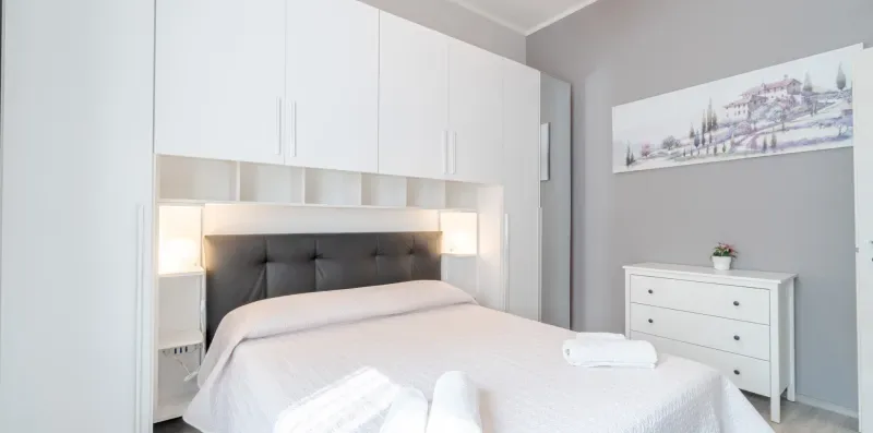 A bedroom with a neatly made bed, built-in white cabinets, and a dresser.