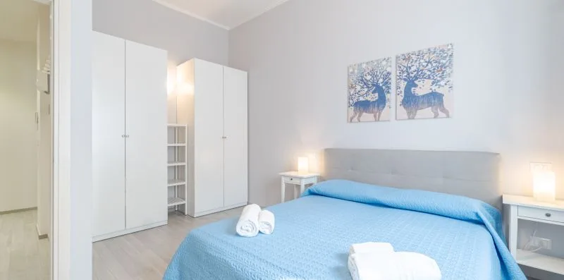 A bedroom with a blue bedspread and white wardrobes.