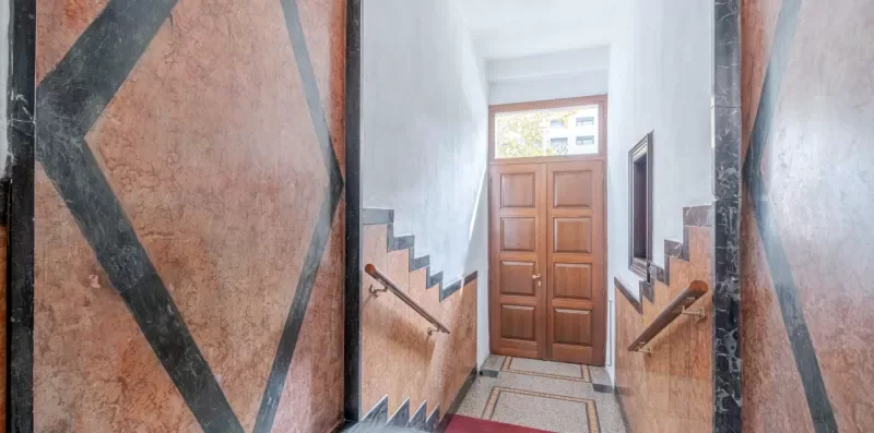 A stairwell landing with a wooden door and decorative patterned walls.