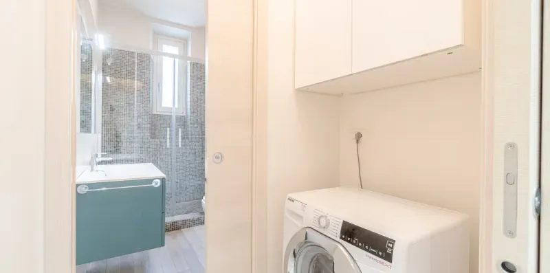 A bathroom with a washing machine beside a glass shower.
