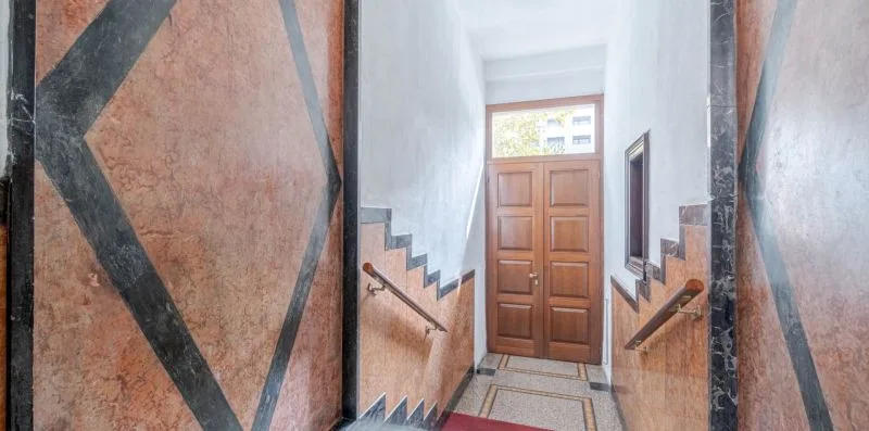 A narrow interior stairwell with patterned walls and a wooden door at the end.