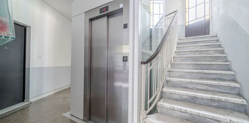 An indoor stairwell with a staircase beside an elevator.