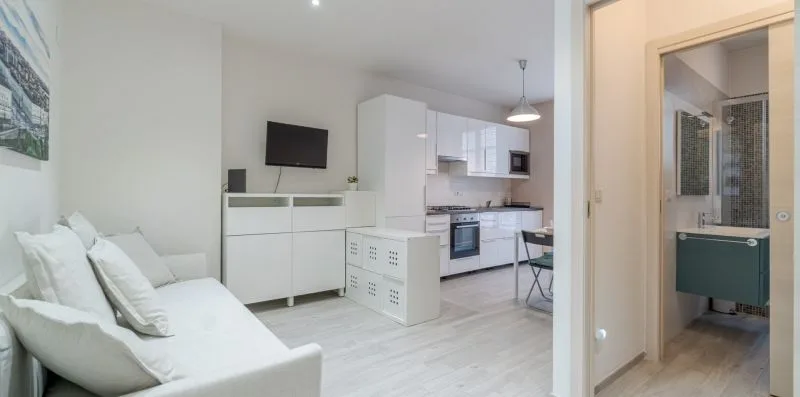 A bright open-plan living area with white seating and a compact kitchen.