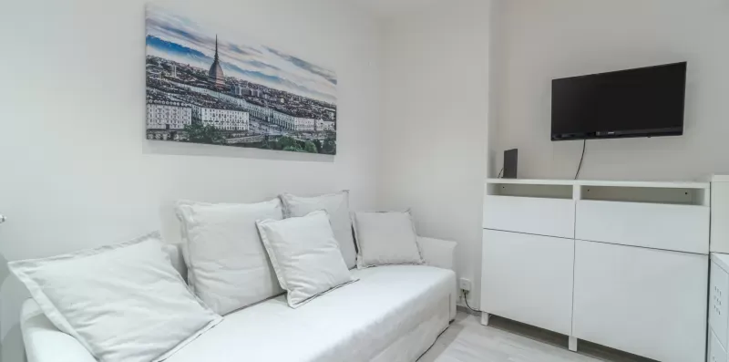 A bright bedroom with a white bed and a wall-mounted television.