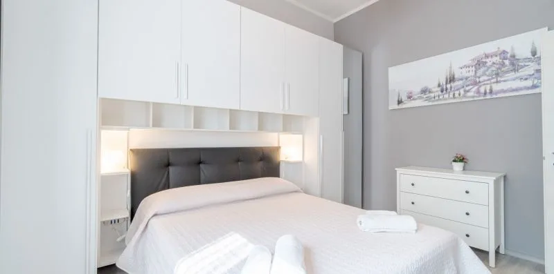 A bedroom with a bed beneath white built-in cabinets and a small dresser.