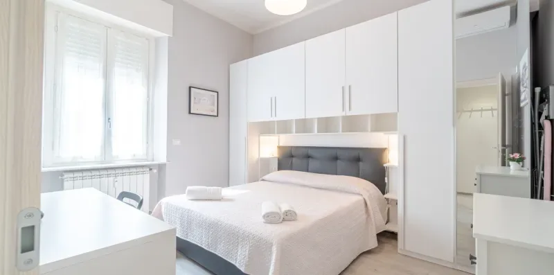 A bright bedroom with a bed, built-in wardrobes, and a large window.