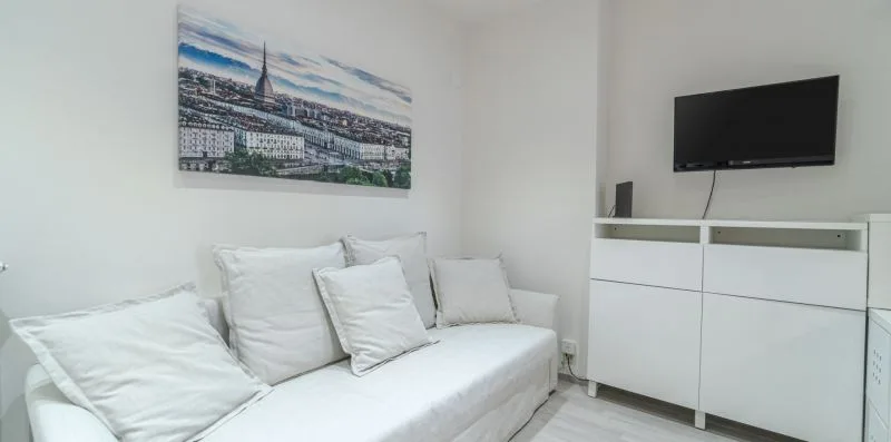 A bright bedroom with a white bed, wall-mounted television, and cityscape artwork.