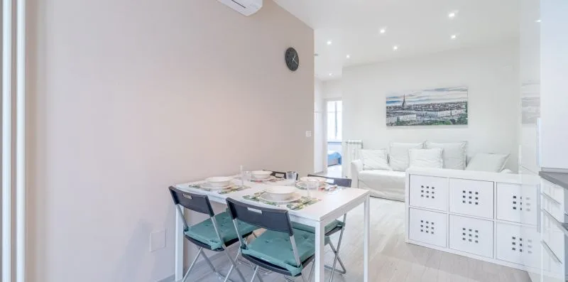A bright dining area opens onto a living space with white seating.