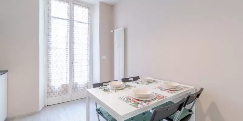 A dining table is set with plates beside tall windows.