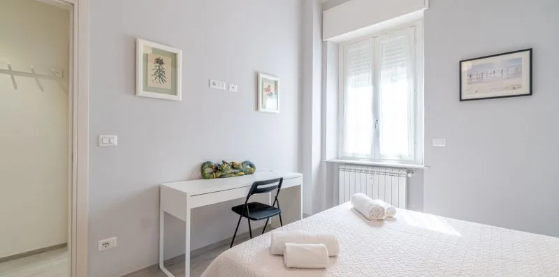 A bedroom with a bed, a desk, and a window.