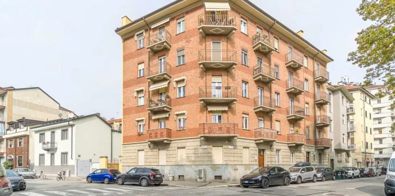 A multi-story brick apartment building with balconies stands along a city street.
