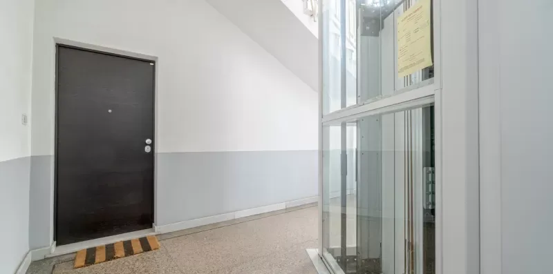 A building hallway with a dark door and a glass elevator.