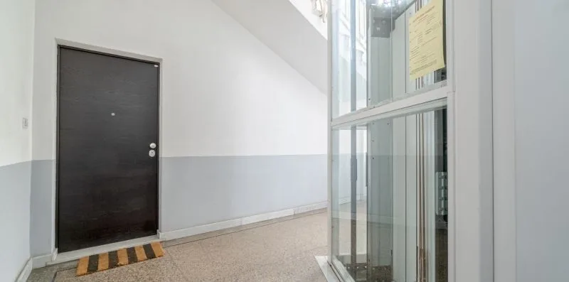 A bright indoor hallway with a dark door and a glass enclosure.