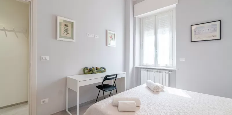 A bright bedroom with a bed, desk, chair, and window.