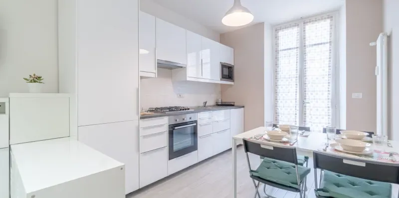 A bright kitchen and dining area with white cabinets and a table by the windows.