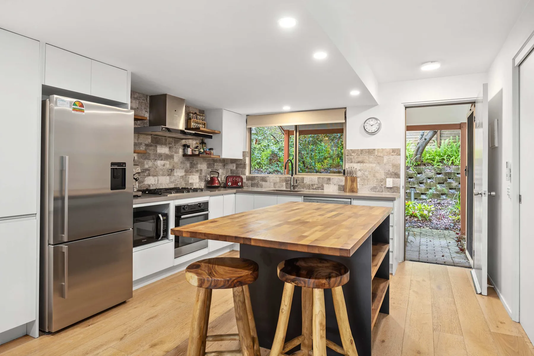 Cocina moderna con una isla de madera y taburetes junto a una puerta abierta.
