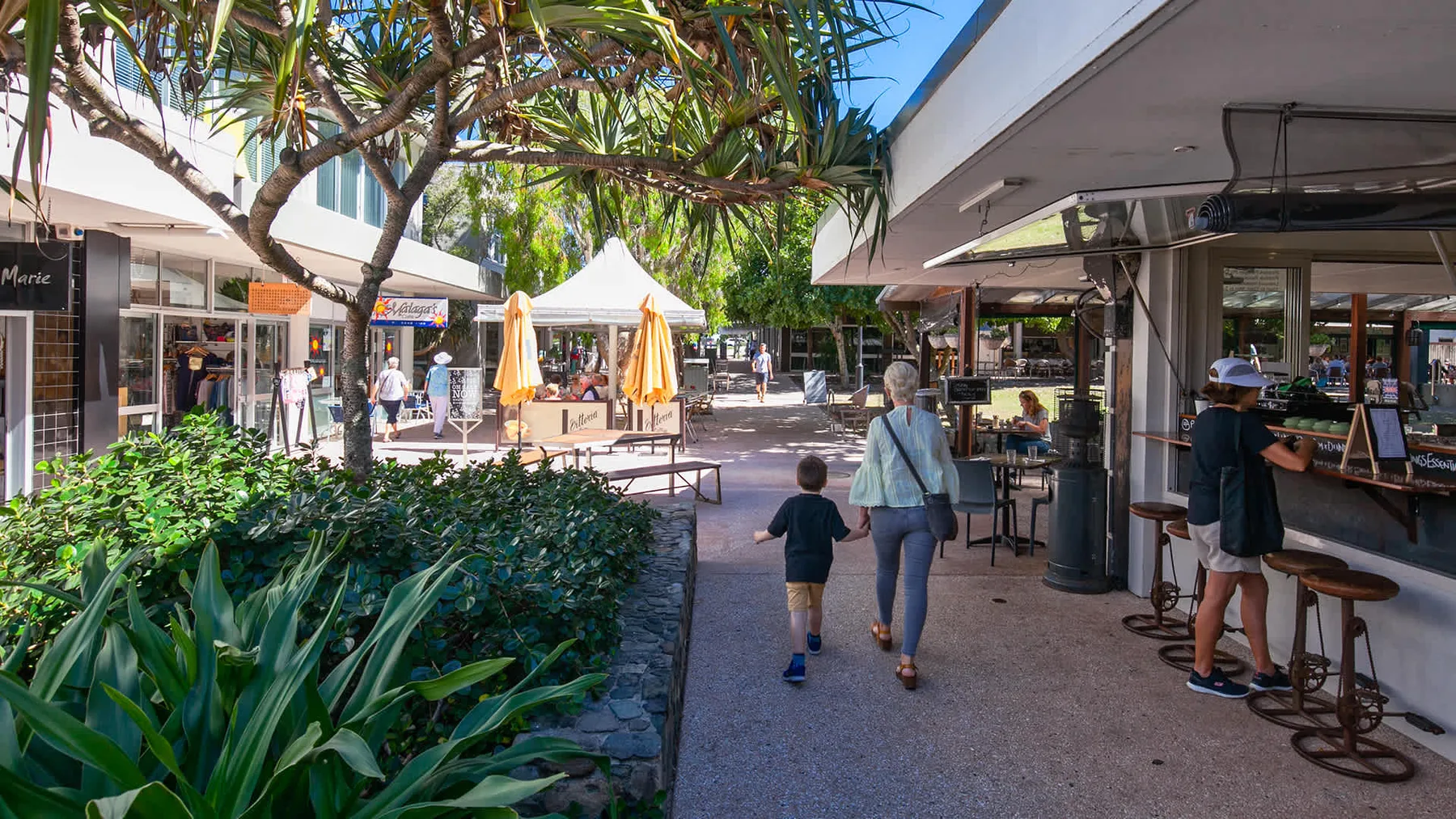 Un paseo peatonal comercial tiene asientos al aire libre y plantas frondosas.
