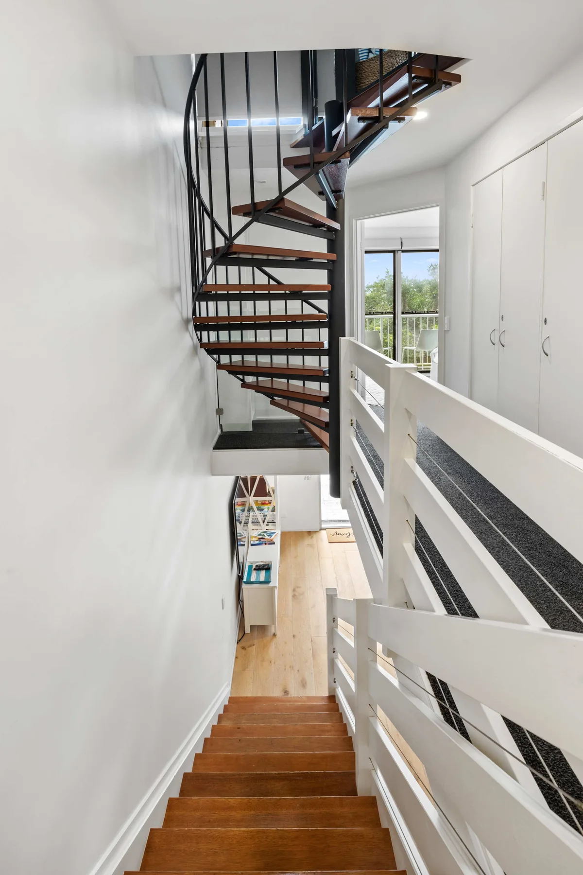 Una escalera desciende junto a una barandilla blanca hacia un pasillo interior luminoso.