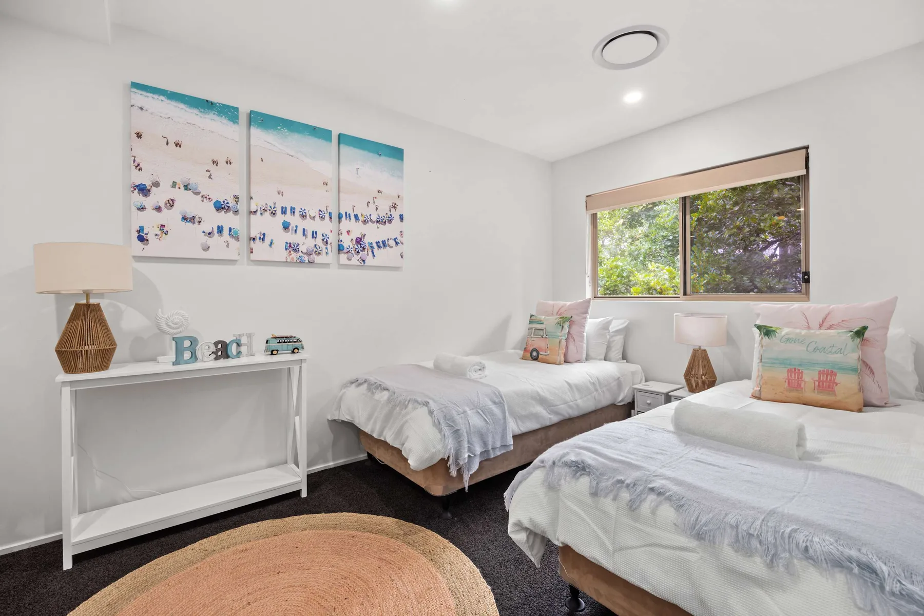 Un dormitorio luminoso con dos camas y una ventana con vista a la vegetación.