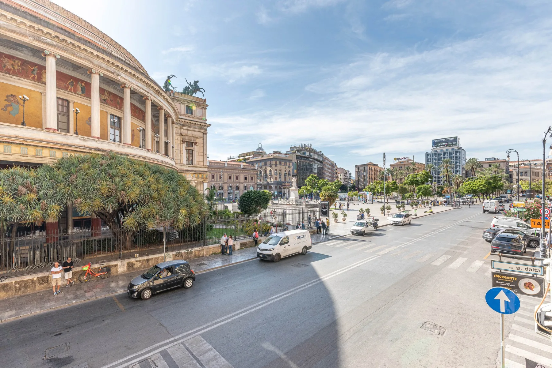 Una amplia calle urbana bordea un gran edificio con columnas y una plaza abierta.