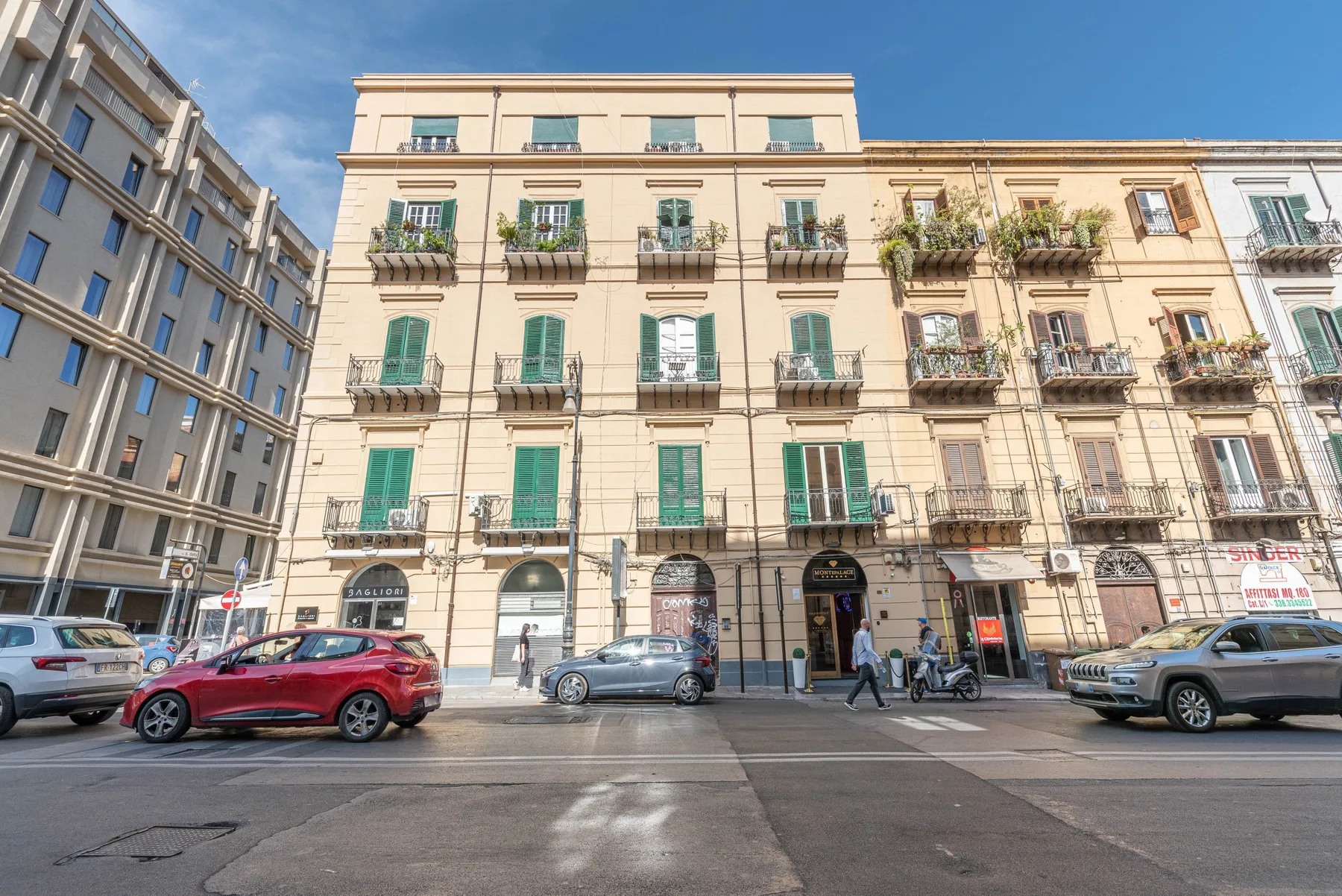 Vista de una calle con un edificio claro, balcones y coches estacionados.