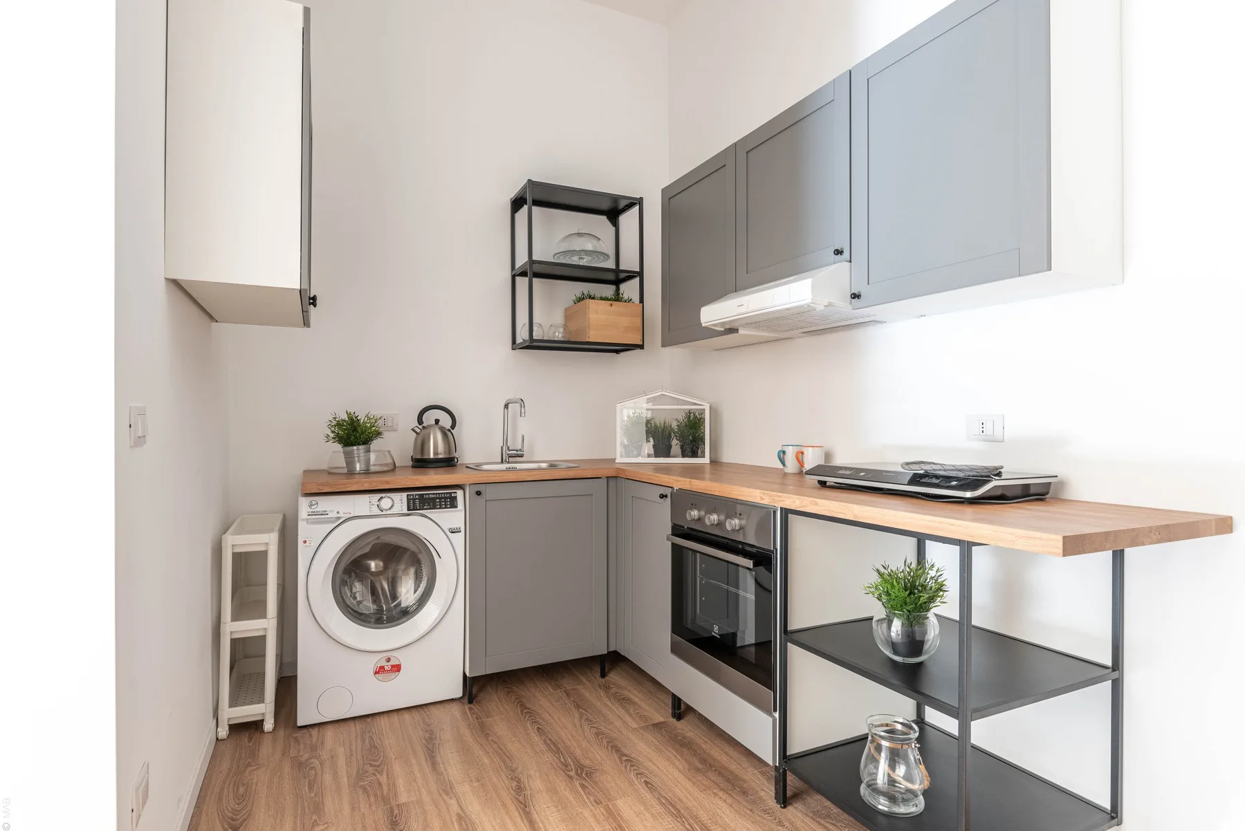 Una cocina luminosa con gabinetes grises, una lavadora y un horno empotrado.