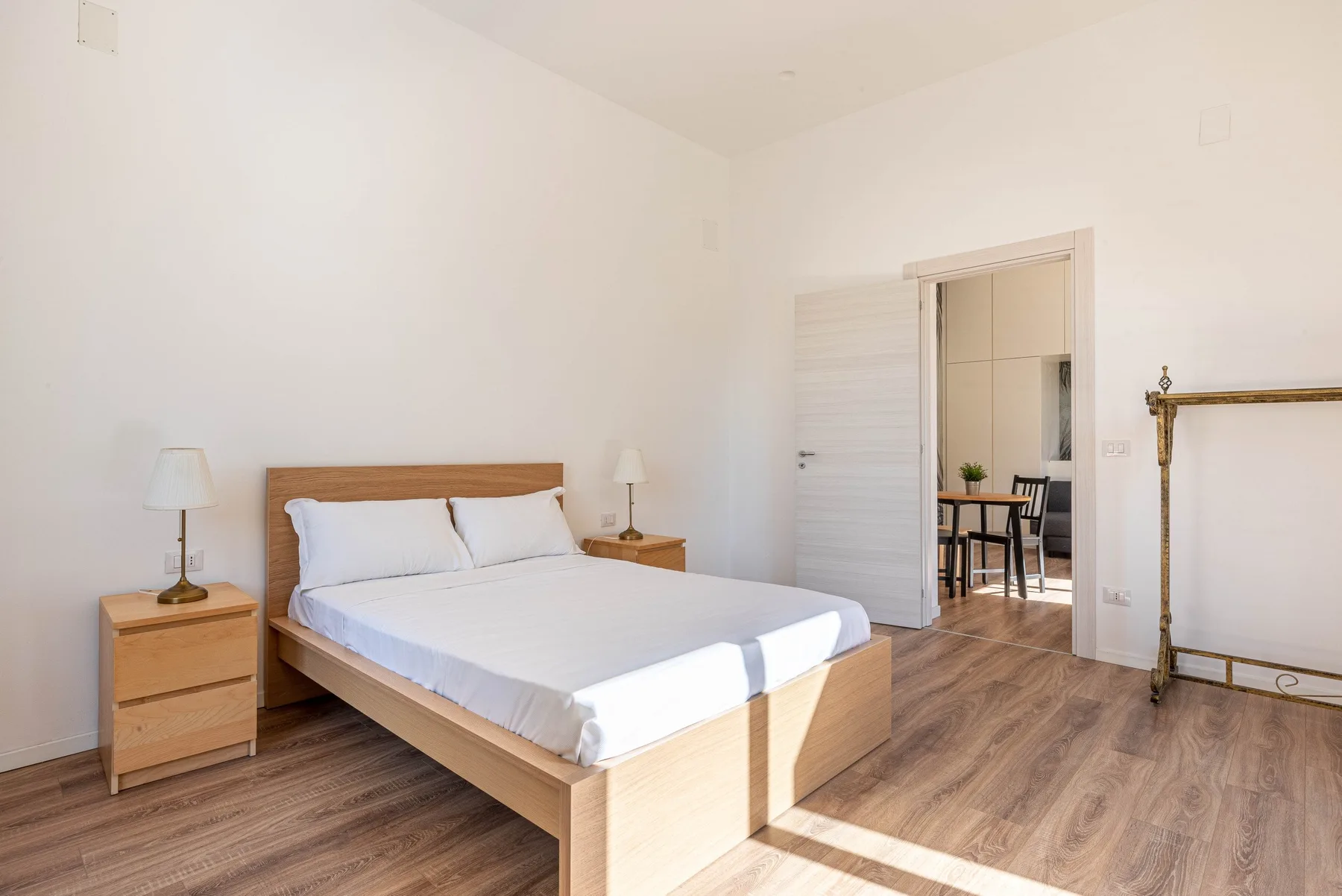Un dormitorio luminoso con una cama de madera y una puerta abierta hacia un comedor.