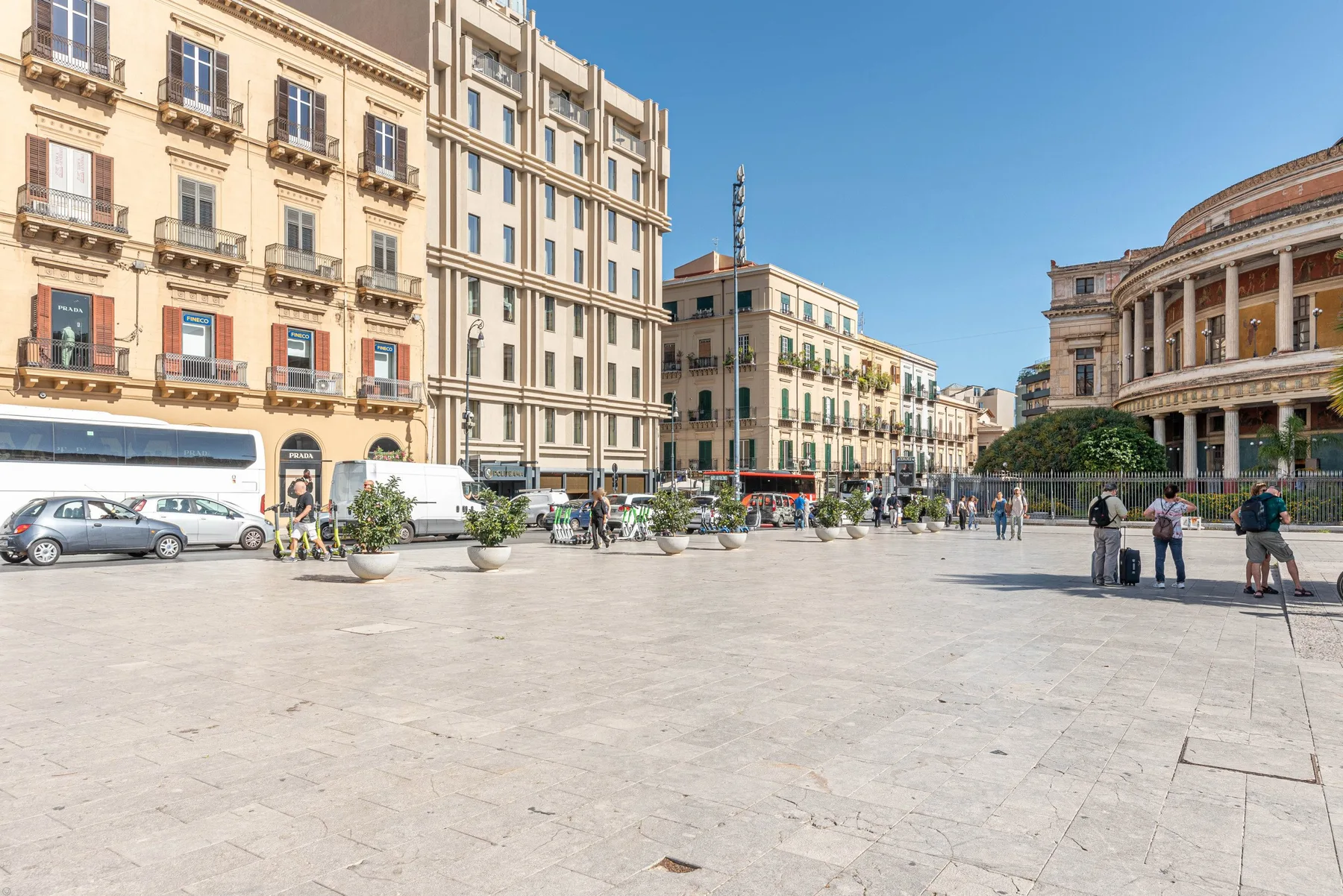 Una plaza urbana con edificios altos, peatones y una fachada curva con columnas.