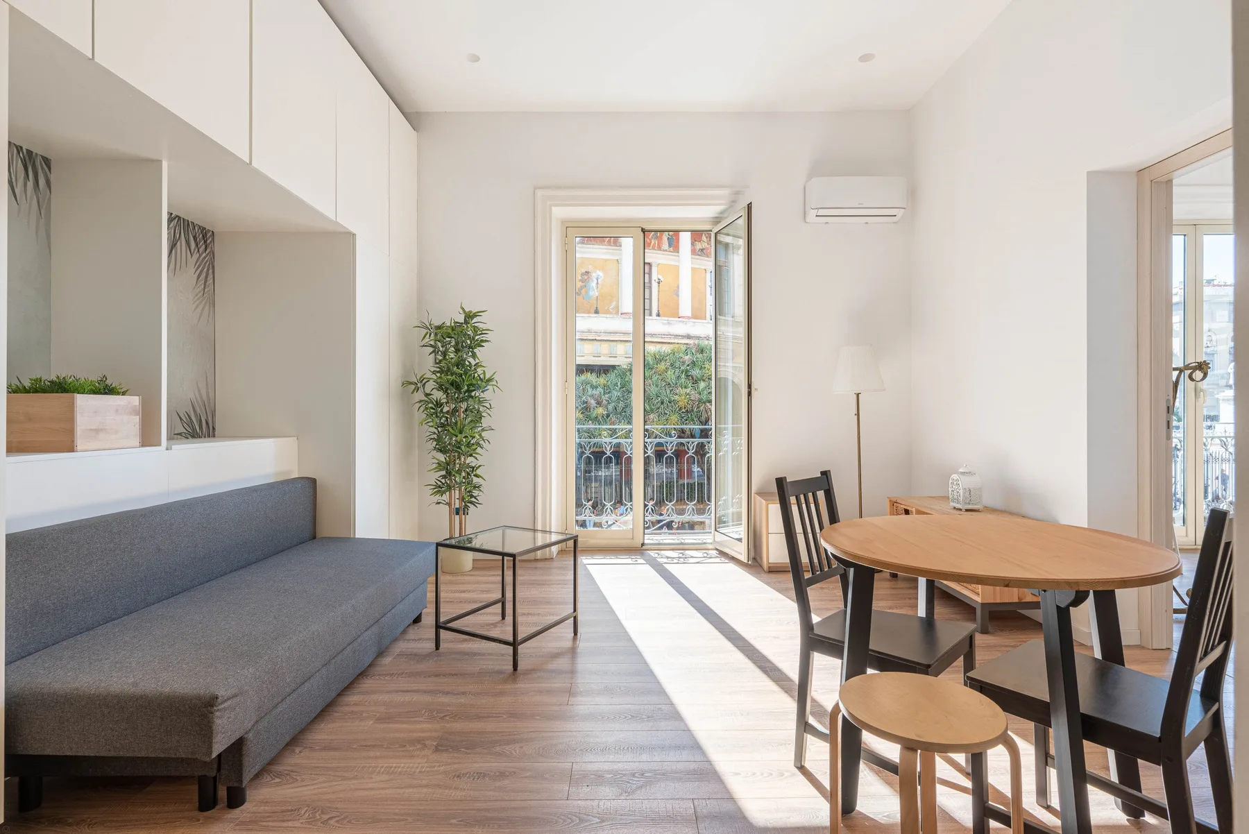 Una luminosa sala de estar y comedor con un sofá gris y una mesa redonda de madera.