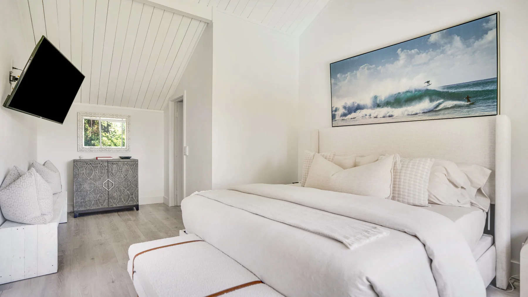 Un dormitorio luminoso con una cama bien tendida y una imagen del océano enmarcada encima.