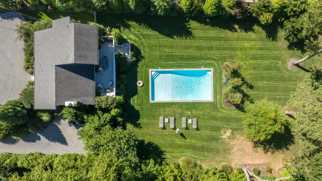 Una vista aérea muestra una piscina y una casa junto a un césped verde.