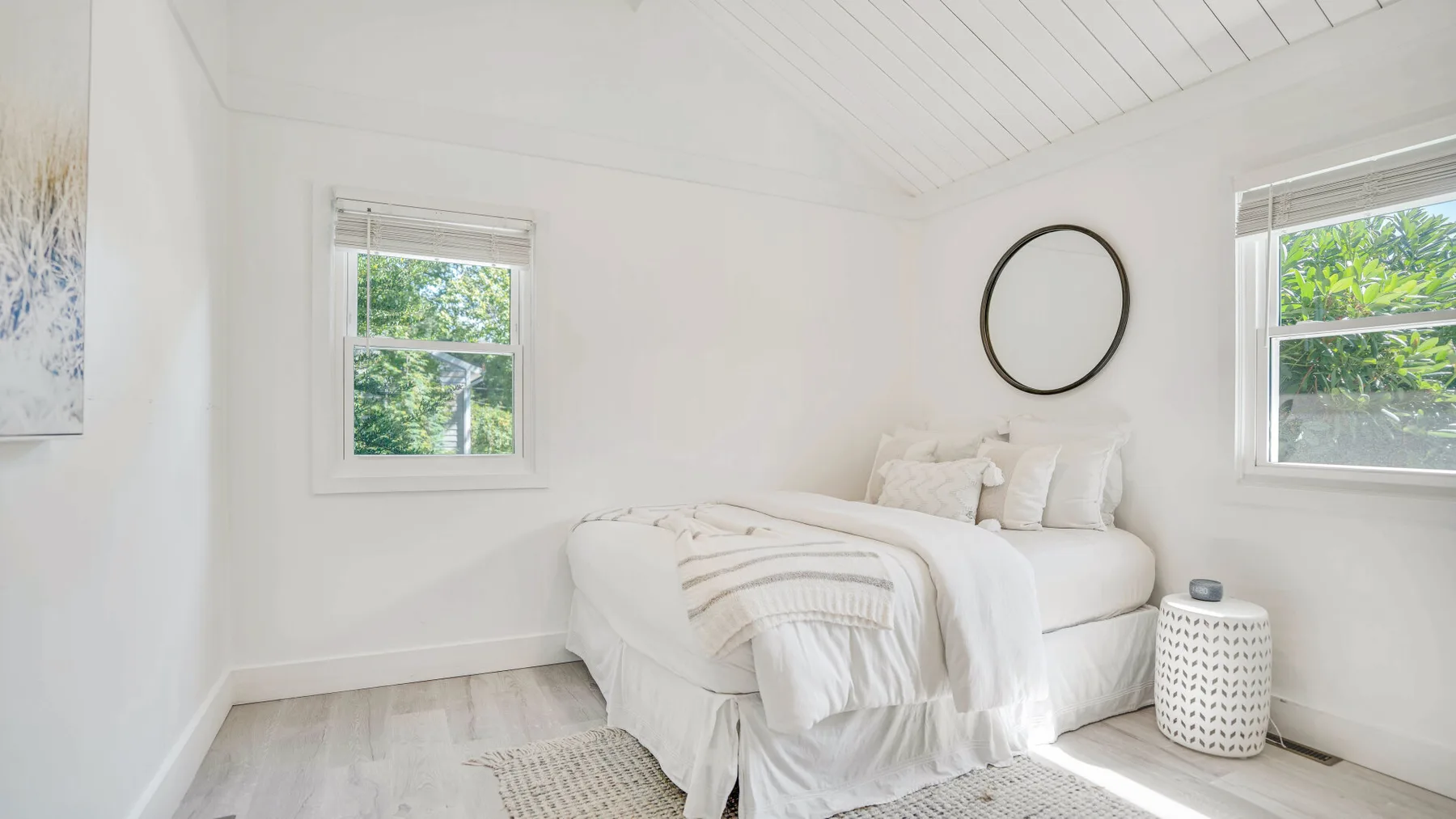 Un dormitorio luminoso con una cama blanca bajo un techo inclinado.