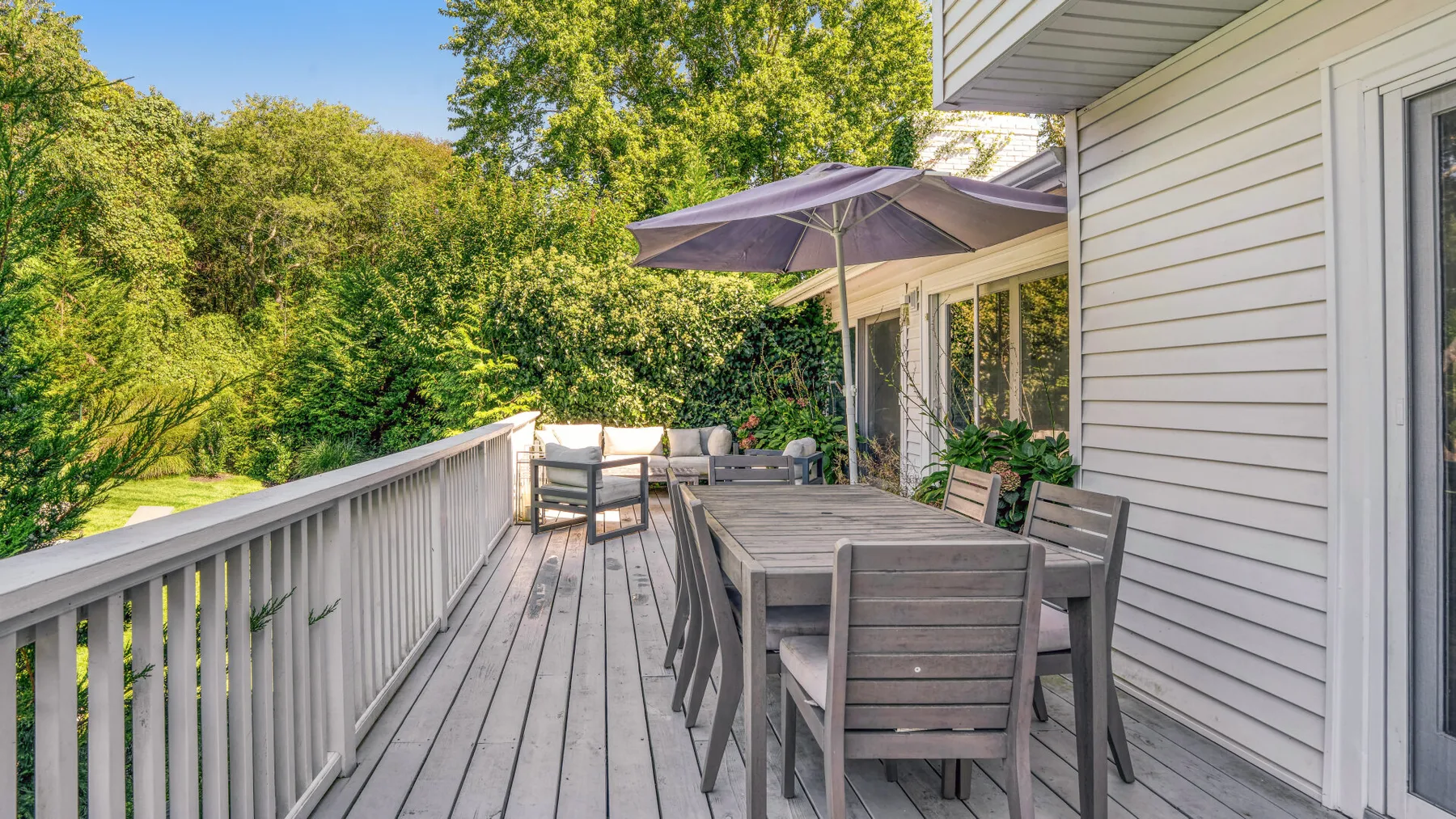 Una terraza exterior con asientos para comer y una sombrilla junto a una casa.