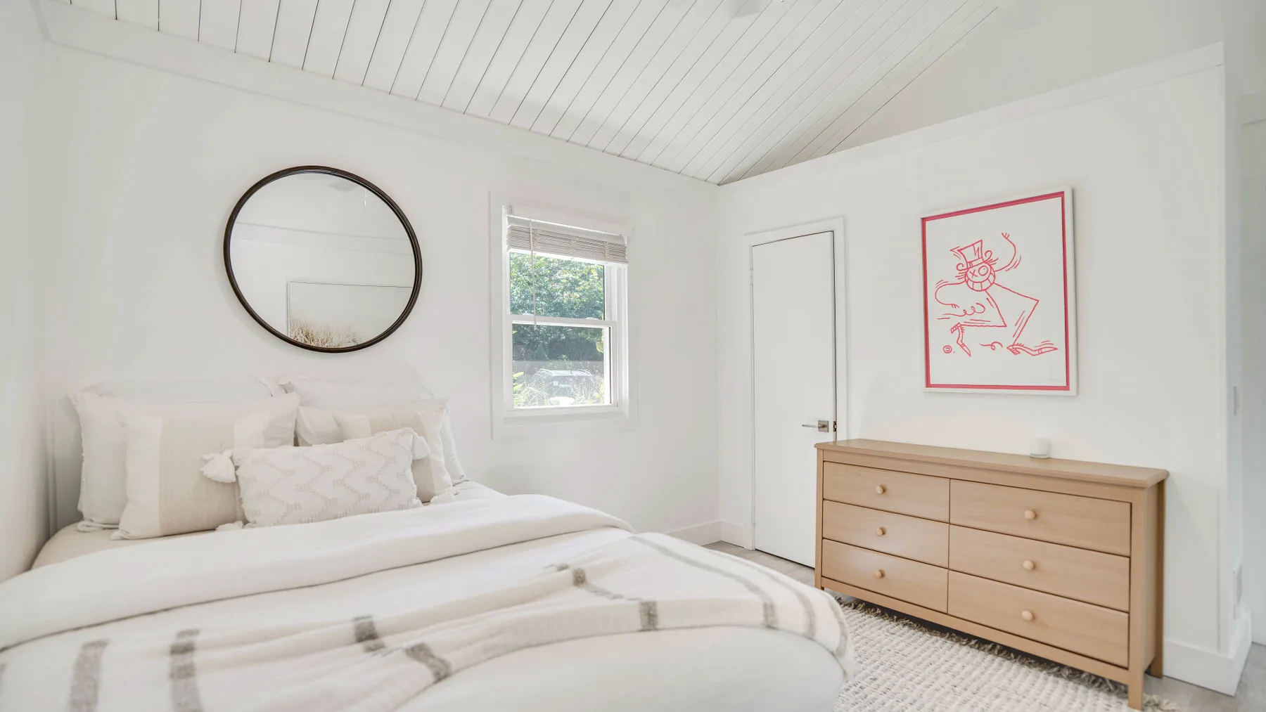 Un dormitorio luminoso con una cama tendida y una cómoda de madera.