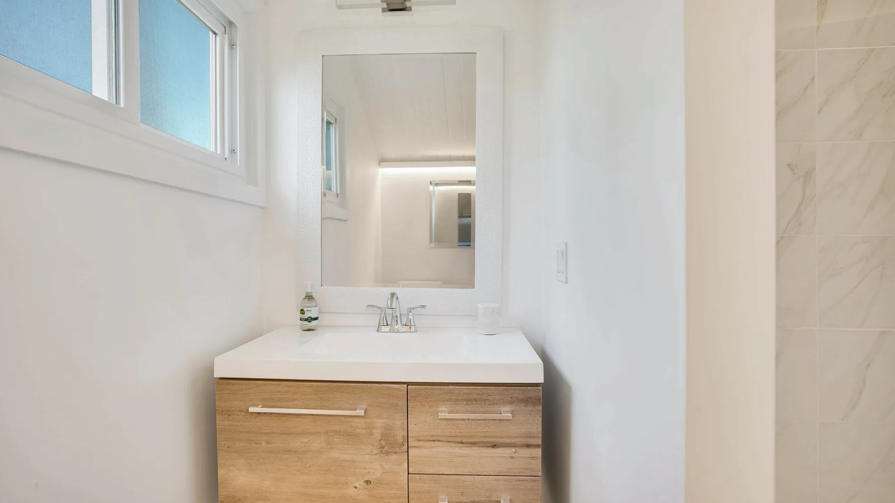 Un lavabo de baño luminoso está bajo un espejo grande junto a una ducha con azulejos.